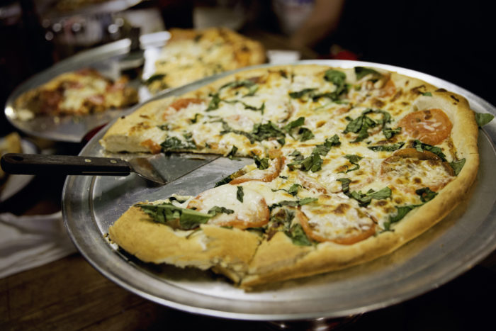 Close up of a pizza on a metal pan with one slice missing, topped with herbs and tomatoes 